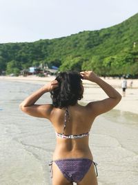 Rear view of woman in bikini standing against waterfall