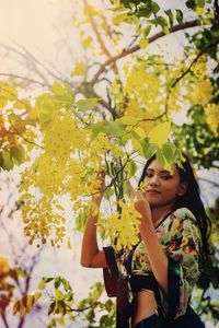 Portrait of young woman standing by yellow flowering plants