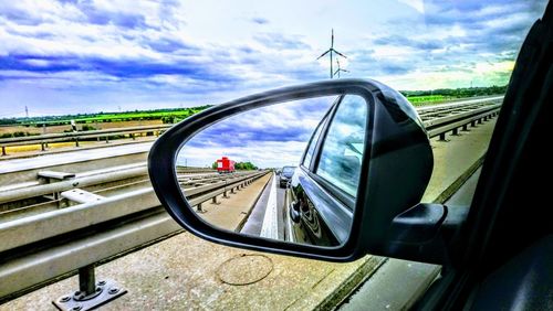 Close-up of side-view mirror against sky