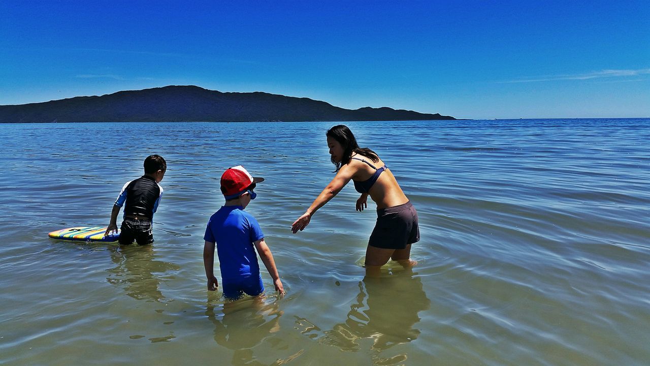 water, leisure activity, lifestyles, togetherness, sea, men, clear sky, vacations, blue, bonding, boys, enjoyment, love, full length, waterfront, family, nature, beauty in nature