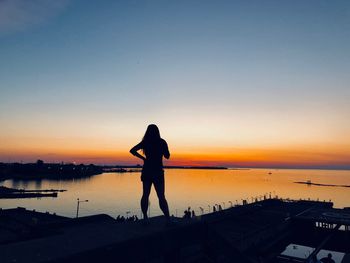 Rear view of silhouette woman standing looking at lake against orange sky
