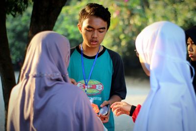 Young man holding woman standing against trees