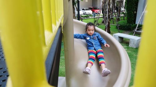 Full length of cute happy asian girl on slide at playground