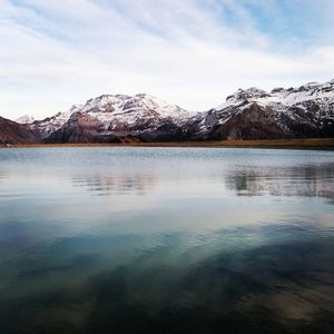 Scenic view of lake by snowcapped mountains against sky