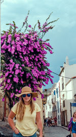 Portrait of young woman wearing sunglasses against pink flower tree