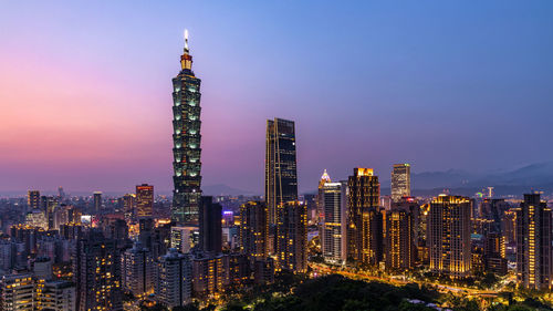 Illuminated modern buildings in city against sky at night