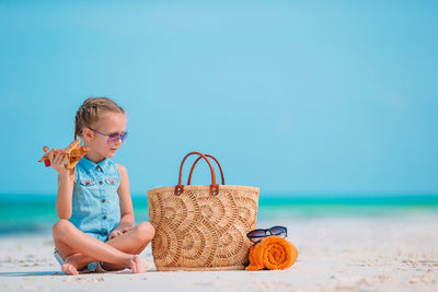 Full length of girl sitting on beach against blue sky