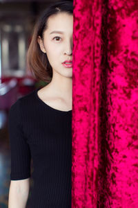 Portrait of beautiful young woman standing behind curtain