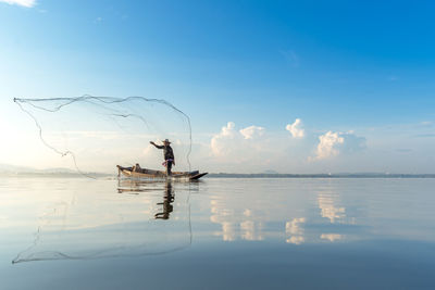 Man on boat fishing in lake against sky