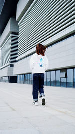 Rear view of boy standing on footpath against building