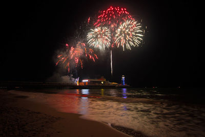 Low angle view of firework display over sea at night