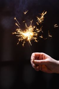 Cropped hand holding sparkler at night