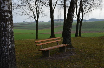 Empty bench on field against sky