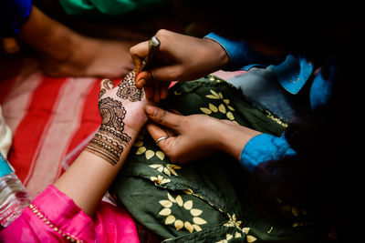 Midsection of artist making henna tattoo on brides hand