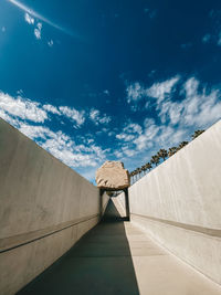 Empty footpath amidst wall against sky