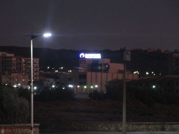 Illuminated street amidst buildings against sky at night