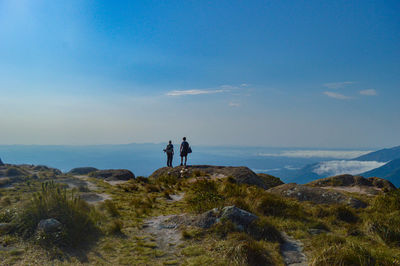 Men standing on rock by sea against sky