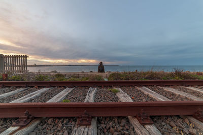 Girl sitting on railroad track by sea against sky