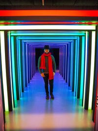 Full length portrait of young man standing against illuminated wall