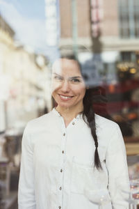 Portrait of smiling female customer seen through glass window