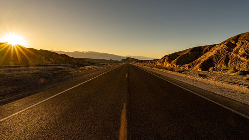 Empty road along countryside landscape at sunset