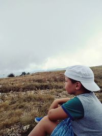 Side view of boy sitting on field against sky