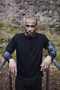 Portrait of confident male athlete leaning on parallel bars in forest