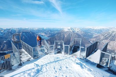 Man leaning on railing against snowcapped mountains and sky during winter