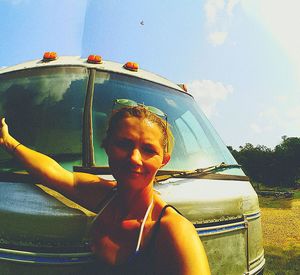 Portrait of smiling young woman sitting by car against sky