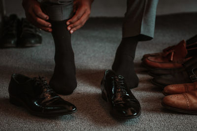 Low section of man wearing his socks surrounded by  shoes