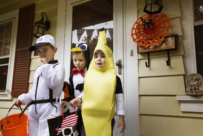 Children in halloween costumes standing against house during trick or treating