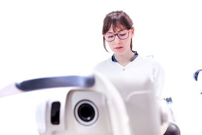 Low angle of concentrated female doctor in uniform working in modern white ophthalmology clinic with keratometer