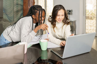 Smiling lesbian women using laptop on sofa at home