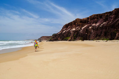 Full length rear view of woman walking at beach against sky