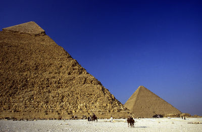 People on desert landscape against pyramids and sky