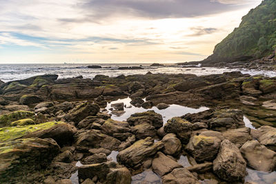 Rocks on beach against sky during sunset