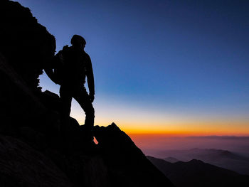 Silhouette people on rock against sky during sunset