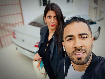 Portrait of man and woman standing against car