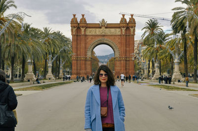 Portrait of woman standing by palm trees against sky