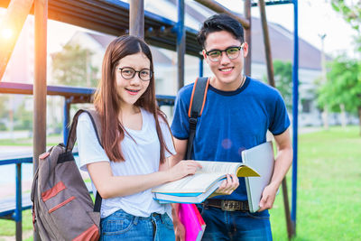 Portrait of smiling friends with books standing at park