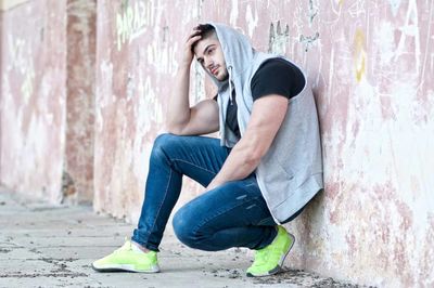 Side view of young man crouching by wall