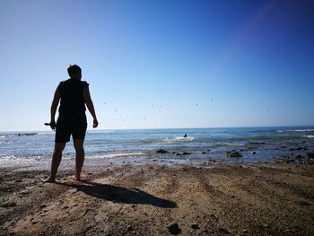 Rear view of man standing at beach against blue sky