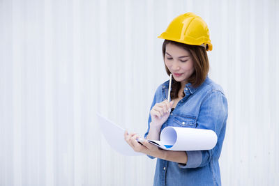 Young woman looking away while standing against wall