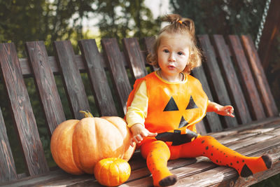 Portrait of cute girl sitting by pumpkin on swing