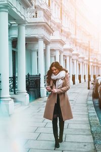 Full length of young woman standing on mobile phone in city