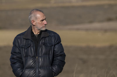 Portrait of adult man in winter clothes standing on fields against blue sky