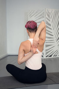 Young fit woman with pink hair, stretching her arms behind her back, on pilates mat.