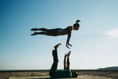 Full length of man balancing woman against clear sky