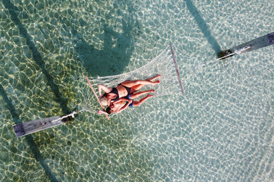 Mother and son relaxing on a hammock over the water. air view.