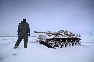 A tank in the snow with one of it crew members walking to it 